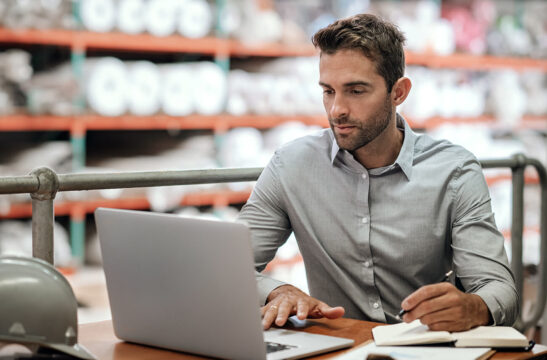 man sitting at computer in warehouse | How to Reduce Facility Management Costs for Good | SLM Facility Solutions Nationwide